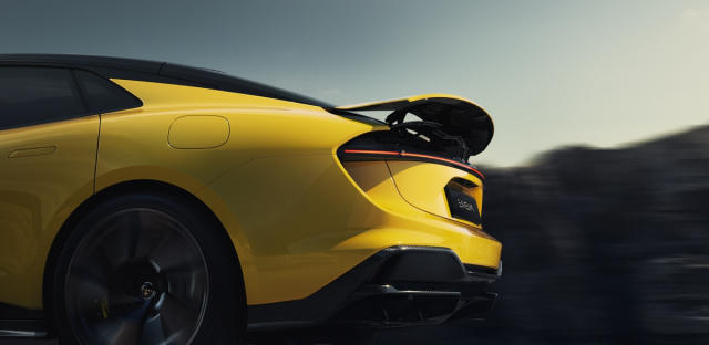 Das Heck eines gelben Lotus Emeya Elektro-SUV ist in Bewegung zu sehen. Der Fokus liegt auf dem aerodynamischen Heckspoiler, den schmalen, durchgehenden Rückleuchten und dem "EMEYA"-Schriftzug. Die dynamische Form des Hecks und die Bewegungsschärfe deuten auf eine Fahrt hin. Der Hintergrund ist verschwommen und zeigt eine helle, möglicherweise bewölkte Umgebung.