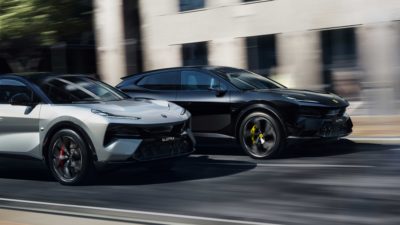 Zwei Lotus Eletre, einer in Weiß und einer in Schwarz, fahren nebeneinander durch eine Stadt.
