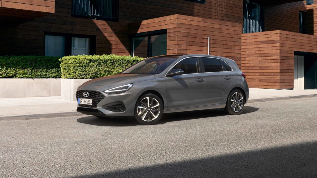 Ein grauer Hyundai i30 steht auf einer Straße vor einem modernen Gebäude mit Holzfassade und begrünten Blumenkästen.