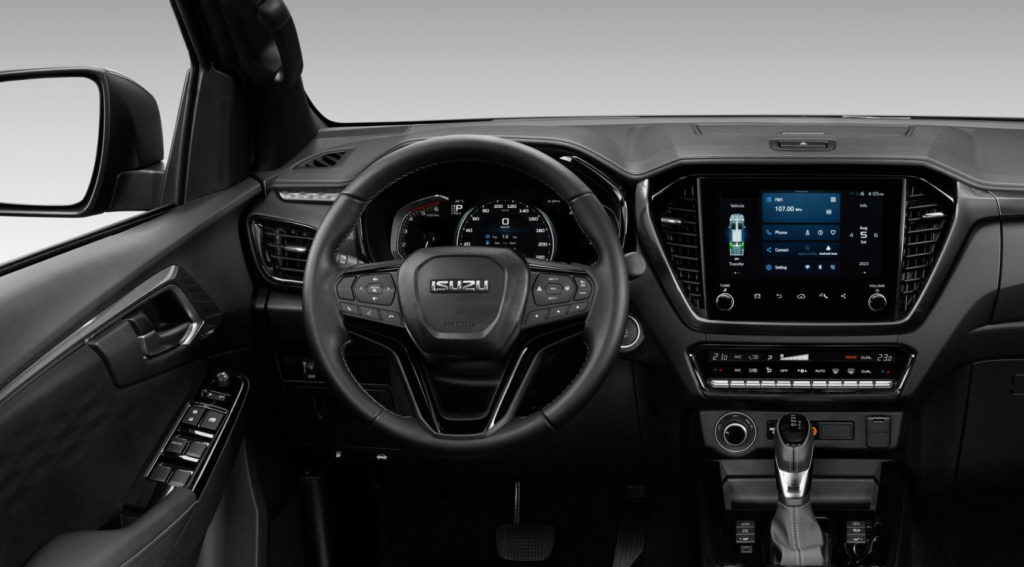 Innenansicht des Armaturenbretts eines Isuzu D-MAX. Das Cockpit ist modern und in dunklen Tönen gehalten, mit einem großen zentralen Bildschirm und einem Multifunktionslenkrad.