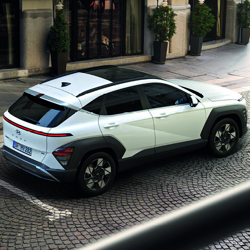 Ein weißer Hyundai Kona mit schwarzem Dach steht auf einer gepflasterten Straße, von hinten schräg fotografiert.