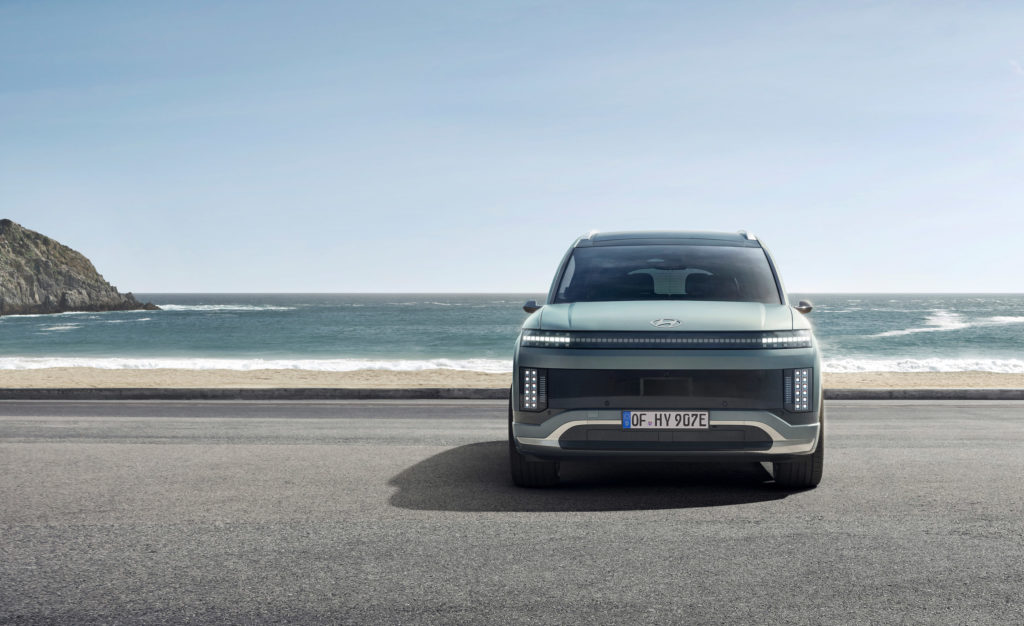 Ein hellgrauer Hyundai steht von vorne gesehen auf einer Straße direkt am Meer. Im Hintergrund sind ein Strand und eine felsige Küste zu sehen.