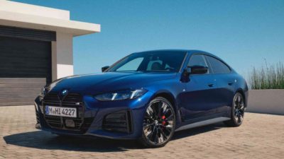 Ein blaues BMW M440i xDrive Gran Coupé steht auf einem gepflasterten Weg vor einem modernen Gebäude.
