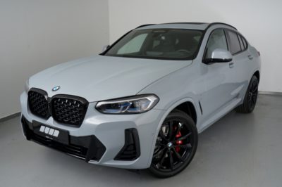 Ein hellgrauer BMW X4 xDrive30d mit schwarzen Felgen und roten Bremssätteln steht in einem Studio.