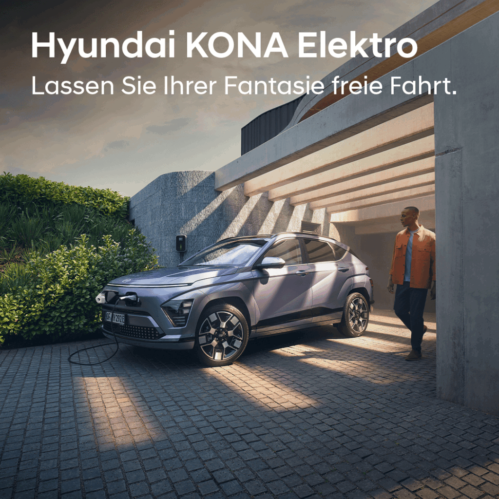 Ein moderner Hyundai KONA Elektro steht in einer stilvollen Hauseinfahrt unter einem Beton-Carport und wird an einer Wallbox geladen. Warmes Abendlicht fällt durch die Architektur und beleuchtet das Fahrzeug. Rechts daneben geht eine Person in Freizeitkleidung am Auto vorbei. Oben im Bild steht der Werbeslogan: „Hyundai KONA Elektro – Lassen Sie Ihrer Fantasie freie Fahrt.“