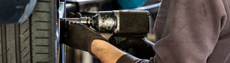 Nahaufnahme eines Mechanikers, der mit einem elektrischen Schlagschrauber die Radmuttern an einem Autoreifen fachgerecht festzieht.