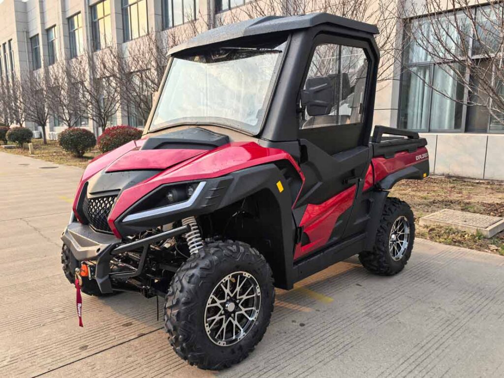 Ein rotes Side-by-Side-Utility-Vehicle mit geschlossener Kabine, markanten LED-Scheinwerfern und grobstolligen Offroad-Reifen auf befestigtem Untergrund.