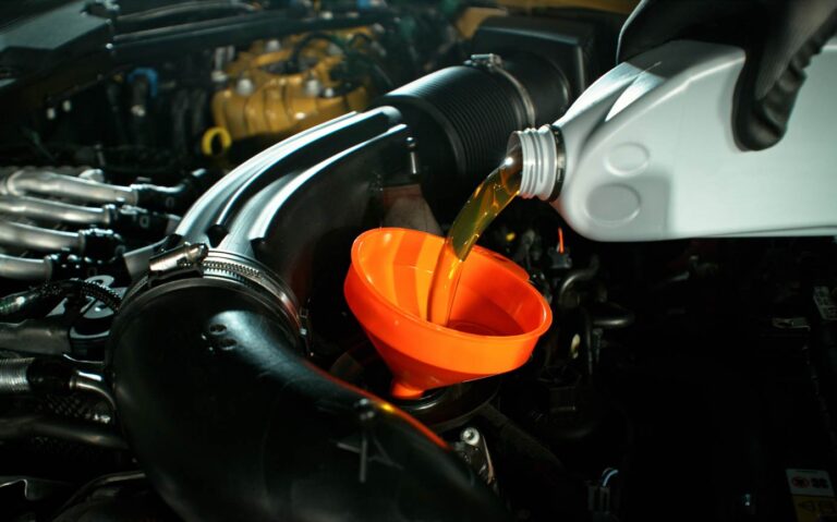Ein Mechaniker füllt in einer Werkstatt Motoröl in einen Automotor ein. Kfz-Wartung, Ölwechsel und professionelles Reparaturkonzept mit dramatischer Beleuchtung.