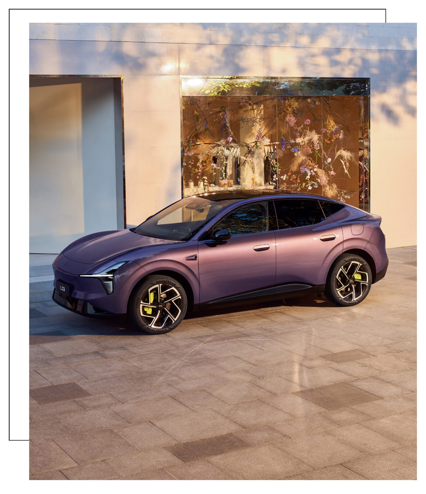 Ein lila Elektro-SUV-Coupé parkt vor einer modernen Gebäudefront mit großem Schaufenster im Sonnenlicht.
